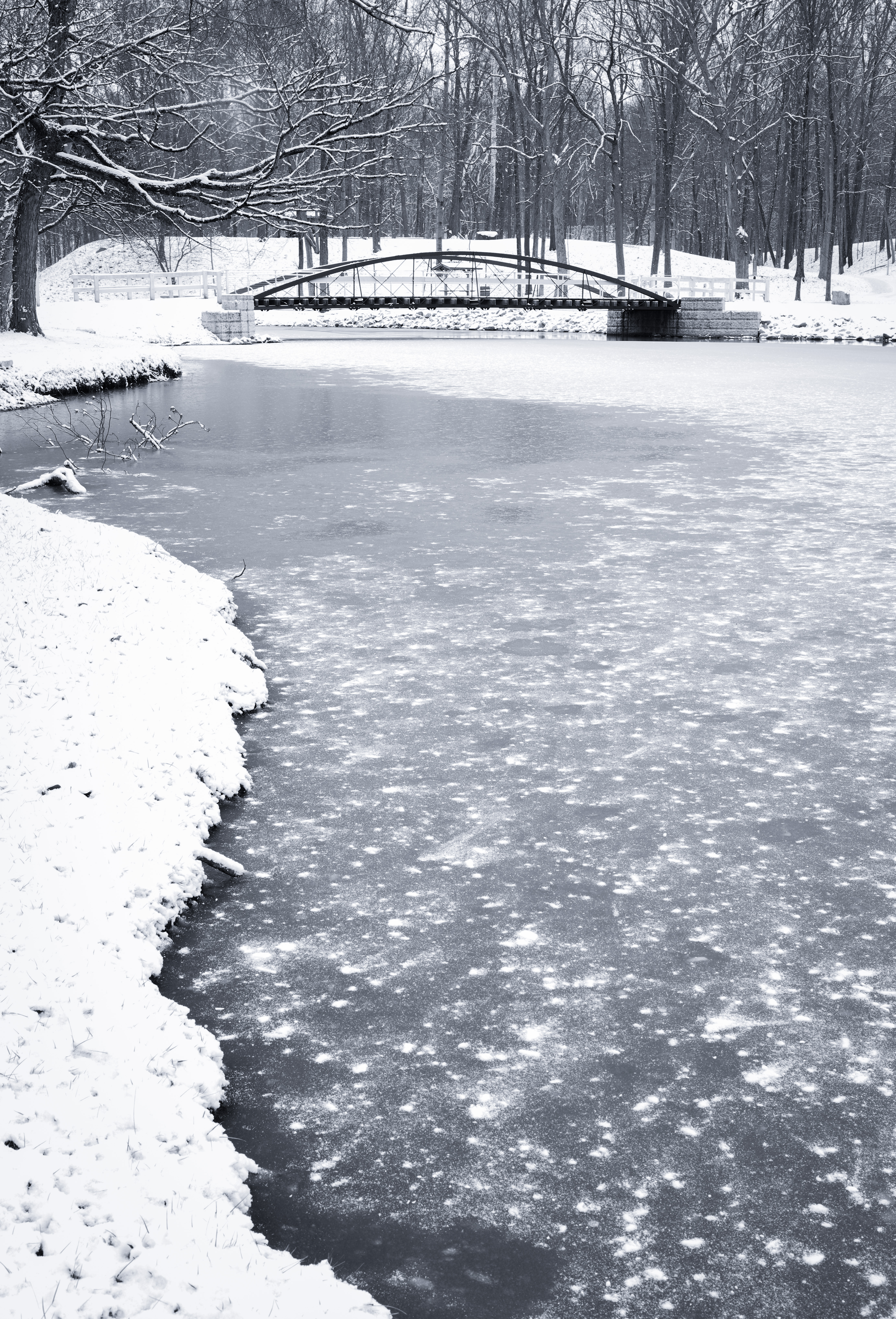 Black and white winter view across frozen water toward an arched bridge at Tawawa Park in Sidney Ohio